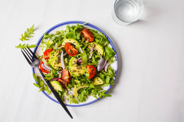 istock Healthy arugula, avocado, tomatoes salad on white marble background. 1069484748