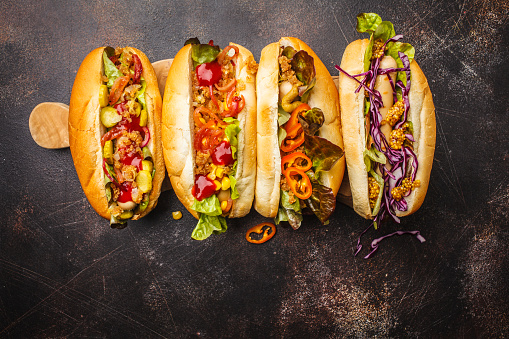 Hot dogs with assorted toppings on a dark background, top view. Traditional american food concept.