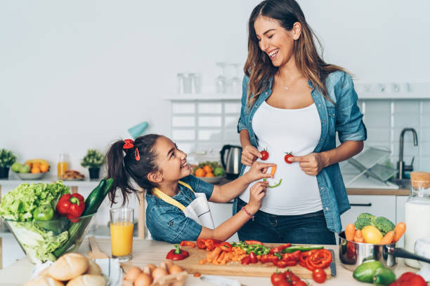 istock Pregnant mother and daughter making vegetable smiley face 1069488308