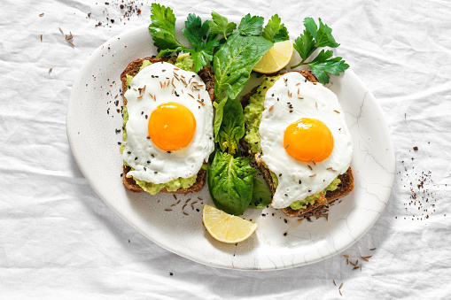 Top view healthy avocado toasts for breakfast or lunch with rye bread, avocado puree toast and fried eggs on white background