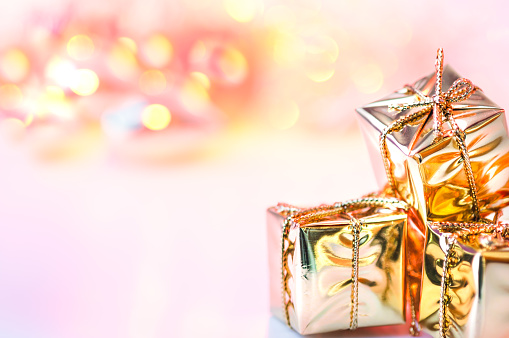 Merry Christmas, New Year, gifts in gold boxes on a background of pink and yellow bokeh.
