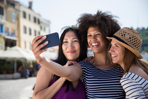 Smiling young friends taking selfie with smart phone at outdoors.