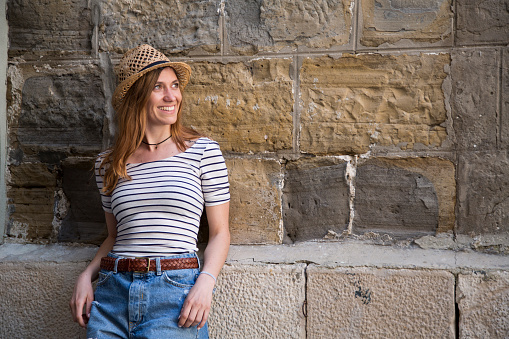 Smiling young woman leaning on wall and looking away.