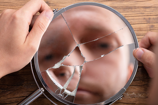 Close-up Of A Man's Face In Broken Mirror Over Wooden Desk