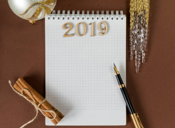 istock clean Notepad sheet,  writing space, fountain pen, Christmas ball, artificial transparent icicle, cinnamon sticks on brown background, top view, lettering 2019 1069511368