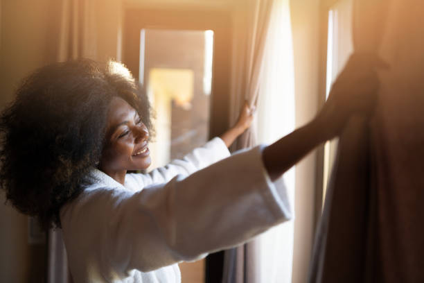 istock Smiling woman opening curtains in hotel room 1069516904