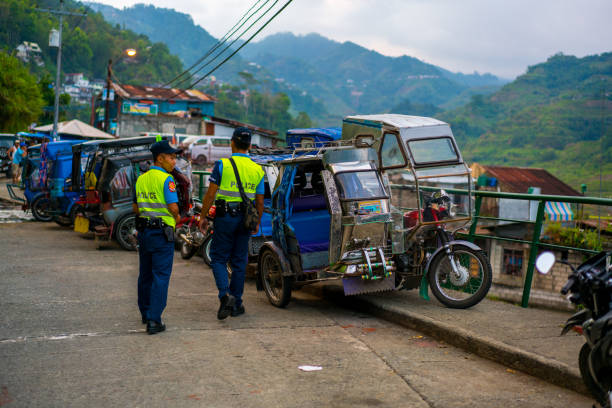 Banaue Street with two police man walking, Ifugao, Philippines Banaue, Philippines - April 28, 2017: Banaue  view showing  tricycles parked in the side of the street and two police men walking on the street, rice terraces, houses, street lights and wire can be seen on the background philippines tricycle stock pictures, royalty-free photos & images
