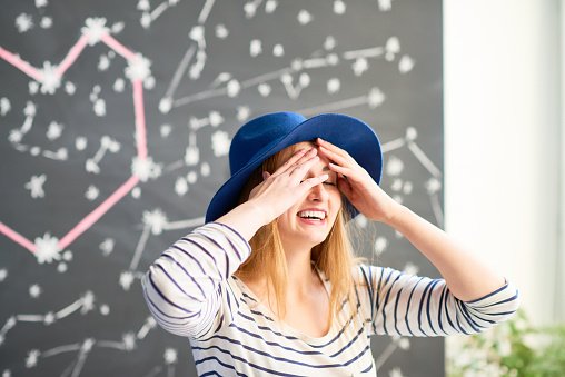Young happy woman standing holding her head and laughing with the blackboard with constellation in the background