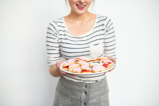 Close-up of woman holding plate with decorated icing heart shaped cookies on white background