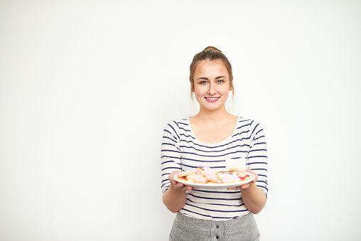 Smiling young girl holding plate with homemade cookies and wants to treat you