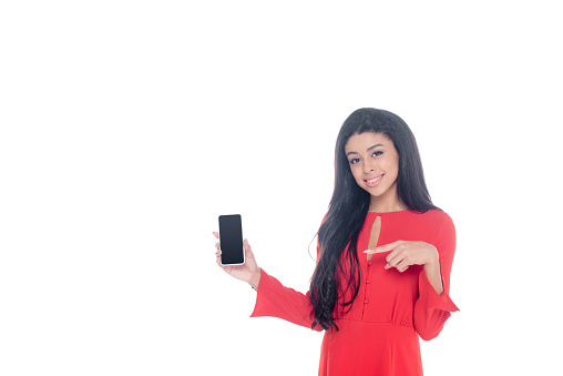 african american woman in red dress pointing at smartphone with blank screen isolated on white