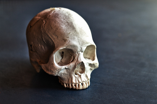 A worn old human skull sits on a black surface.