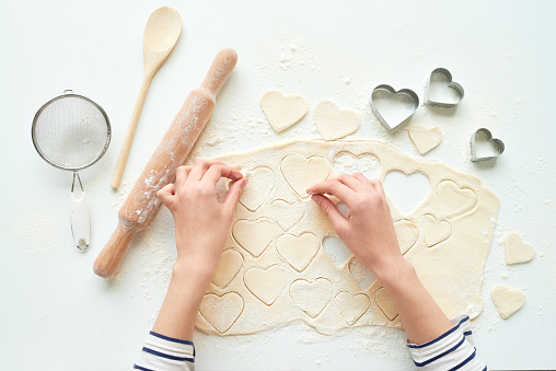 Close-up of young woman baking cutter cookies heart shape for Valentine's Day