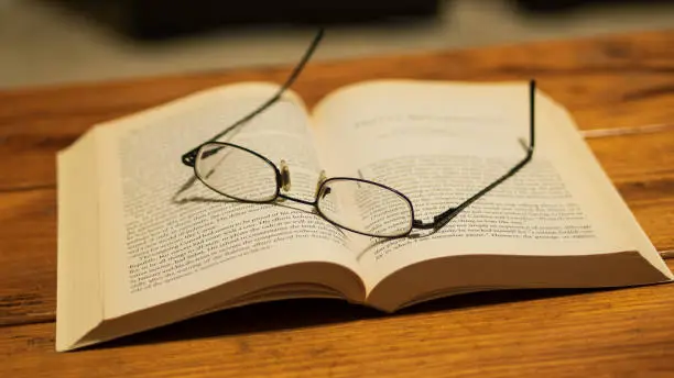 Eye glasses resting on top of a book, sitting on a wooden coffee table