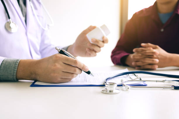 istock Confident doctor man holding a pill bottle and writing while talking with senior patient and reviewing his medication at office room. 1069538430