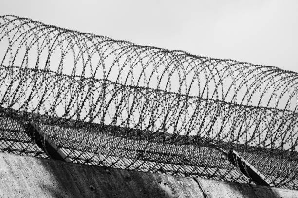 istock Barbed wire rolls on the wall edge of a prison in Germany, black-and-white 1069540618
