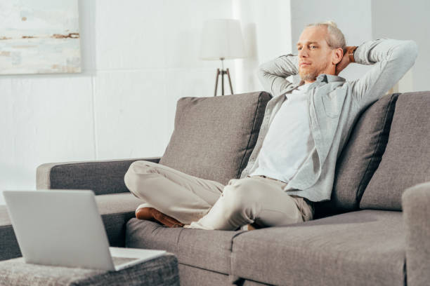 istock handsome behind man sitting with hands behind head on couch and looking at laptop 1069544284