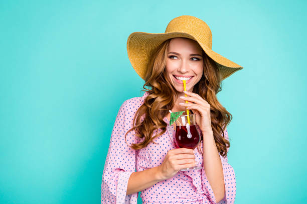 attraente bella bella bella bella bella splendida signora con panama in testa il suo stile elegante a onde riccie acconciatura alla moda che guarda da parte tenere la bevanda in mani isolate su uno sfondo turchese luminoso - pink hat foto e immagini stock