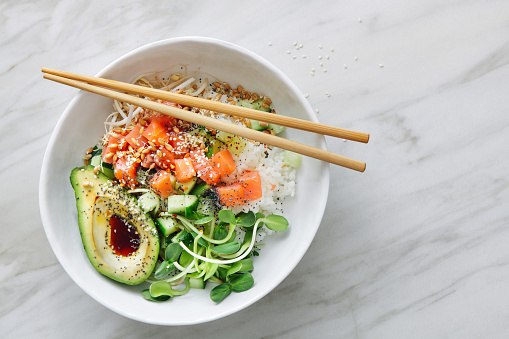 Poke bowls with salmon, avocado, vegetables, sprouts and ponzu dressing on marble background