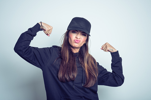 Studio portrait of young woman wearing black clothes and baseball cap, clenching fists.
