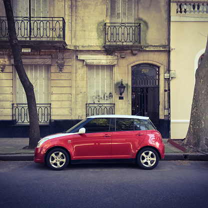 Buenos Aires, Argentina - September 17, 2017: Brand new red Suzuki car parked next to sidewalk and old style house. The city is full of contrasts like this one