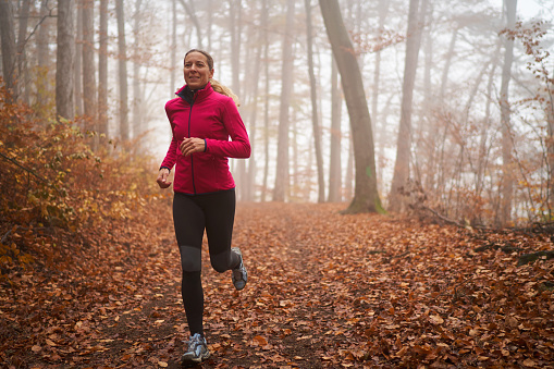 45 year old woman running in autumn forest foggy bad weather conditions cold october or november look