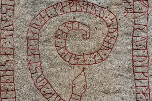 Old rune stone with red runes chiseled in the shape of a long snake