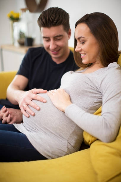 istock Pregnant Couple Sitting On Sofa With Man Touching Womans Stomach 1069560106