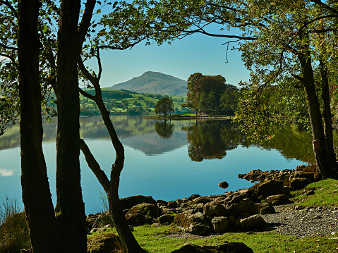 Picturesque landscape scene of Bala lake with clear blue sky, shoreline and mountains reflected on the water. In the distance is the ridge of Aran Benllyn with the peak of Aran Fawddwy on the skyline.
