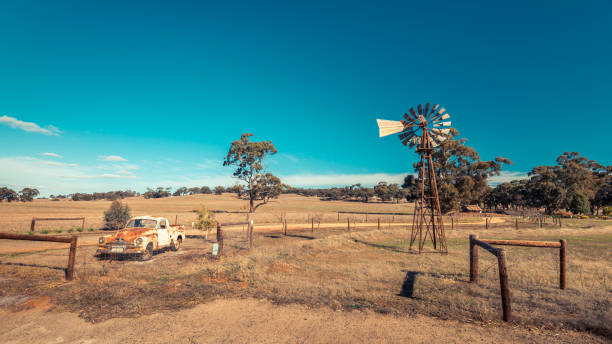 Kapunda, South Australia - June 17, 2017: Rusty Holden FJ Ute and vintage Kookaroo windmill on display near farm entrance from highway