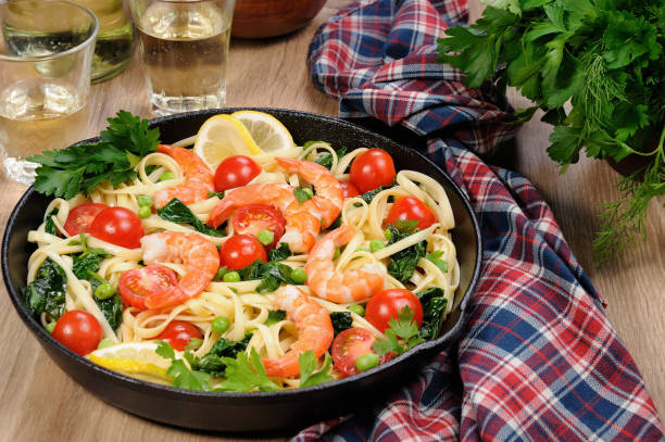 pâtes aux crevettes frits, petits pois, tomates et épinards dans une poêle, sur une table avec des verres de cidre. - carbohydrate diabetes pasta food photos et images de collection