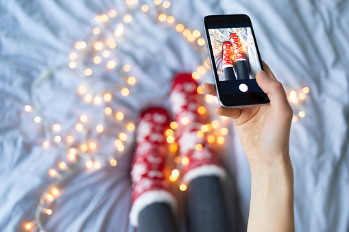 Woman taking photo of her legs in christmass socks and lights, on bed.