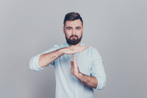 gros plan de portrait en studio photo de sérieux avec soies brunet chaume mal rasé en regardant l’homme caméra faire donner le temps à fond fond gris geste isolé - signe de temps mort photos et images de collection