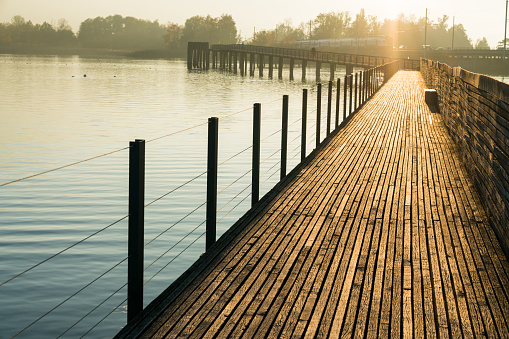 long wooden pier and boardwalk over Lake Zurich near Rapperswil in golden evening light with silhouette of mountains in the background