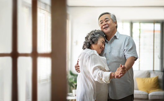 Cheerful Asian Senior couple dancing and smiling at home. Copy space.