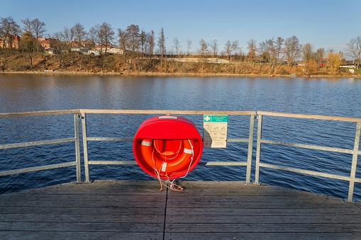 Red lifebuoy hanging on wooden pier, Jordan pond, Tabor, oldest dam in the Czech Republic, sunny autumn day, life insurance concept