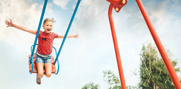 счастливая маленькая девочка смеется и качается на качелях в городском парке летом - child swing swinging playing стоковые фото и изображения