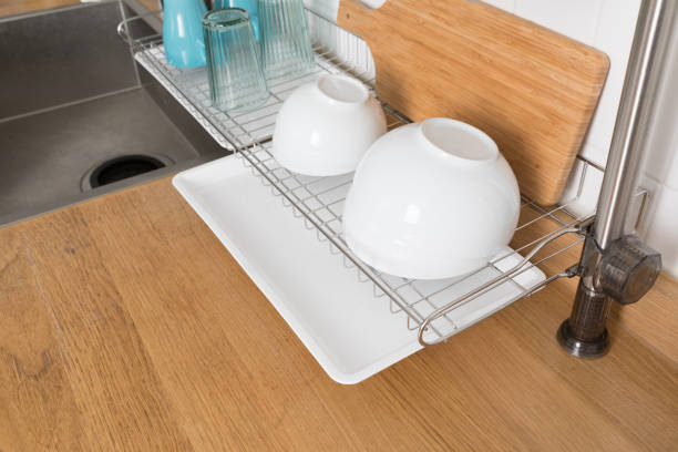 istock Clean dishes drying on metal dish rack on light background. Kitchen utensils and dishware on wooden shelf. Kitchen interior background.Text space. 1069622022