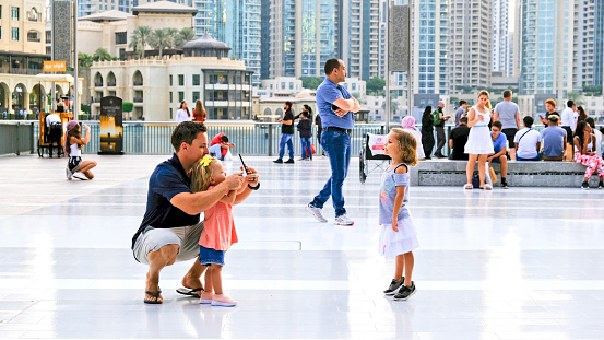 Dubai, United Arab Emirates - 31 October, 2018: Tourist are gathering on the Dubai mall square. A small girl is posing for her father and sister while they are taking pictures.