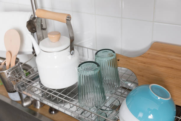 istock Clean dishes drying on metal dish rack on light background. Kitchen utensils and dishware on wooden shelf. Kitchen interior background.Text space. 1069622784