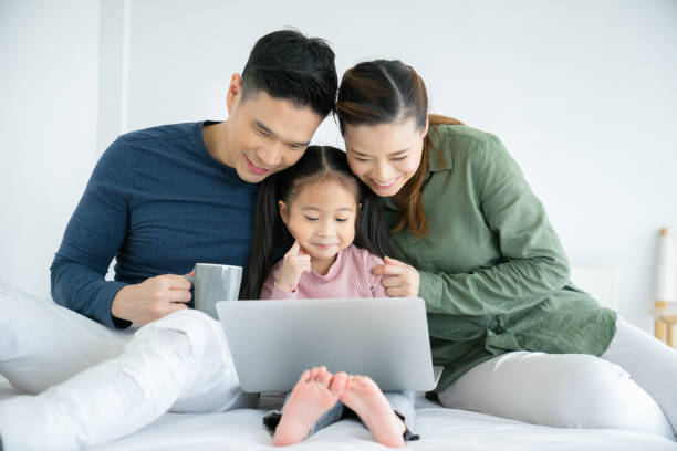 Parents having fun with their little daughter on bed with tablet. stock photo