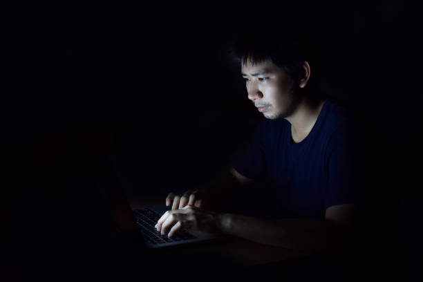 istock Asian man using laptop in the black dark room and working late at night 1069643794