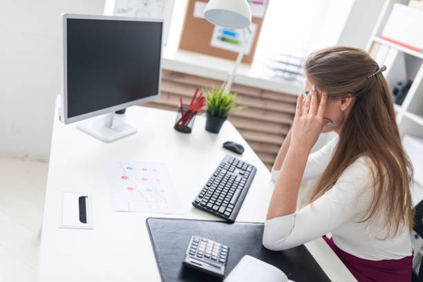 istock A young girl sitting at a computer table and holding hands on his head. 1069649972