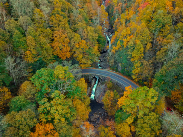Aerial Drone view of waterfall in Autumn / fall in the Blue ridge of the Appalachian Mountains near Asheville, North Carolina. Vibrant red, yellow, orange leaf foliage colors on the curve of mountain road side. stock photo