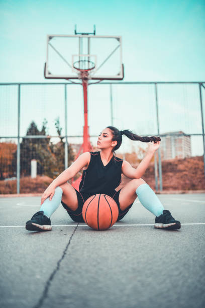 istock Cute Female Basketball Player Posing While Sitting On A Basketball Playground 1069650596