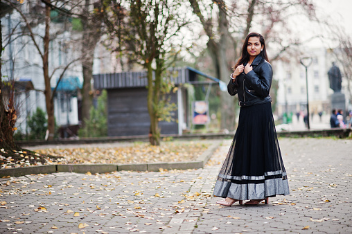 Pretty indian girl in black saree dress and leather jacket posed outdoor at autumn street.