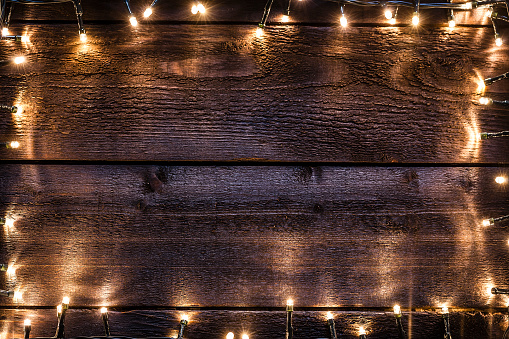 Top view of an empty rustic wooden table with Christmas string lights are all around the border making a glowing frame and leaving useful copy space for text and/or logo. Predominant color is brown. Low key DSRL studio photo taken with Canon EOS 5D Mk II and Canon EF 100mm f/2.8L Macro IS USM.
