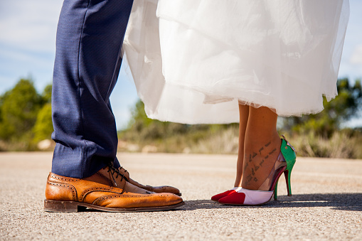 Feet of a newlywed couple facing each other in the middle of the asphalt of a lonely road on a sunny day in a rural location outdoors