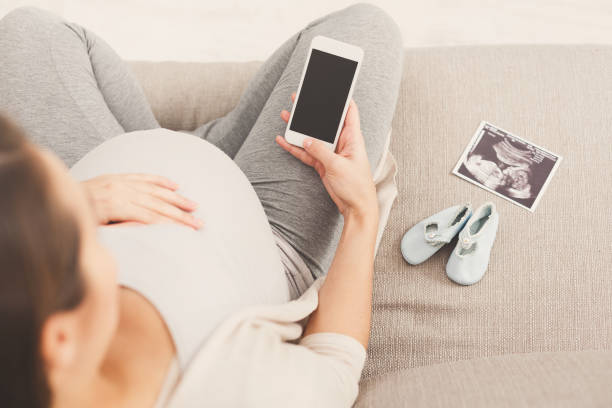 szczęśliwa kobieta w ciąży za pomocą smartfona w domu - human pregnancy telephone ultrasound family zdjęcia i obrazy z banku zdjęć