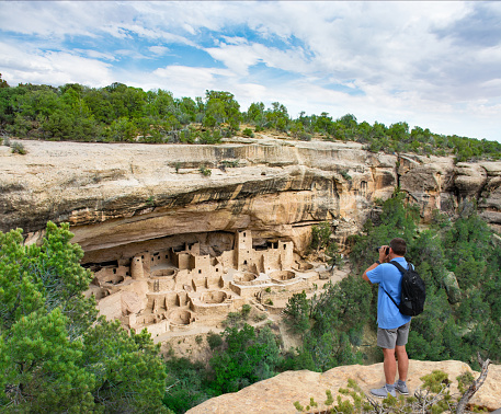 Man on vacation using his camera. videotaping historical cliff dwellings. Ancestral. Puebloan archaeological sites. Cliff Palace ruins at Mesa Verde National Park, Colorado, USA.